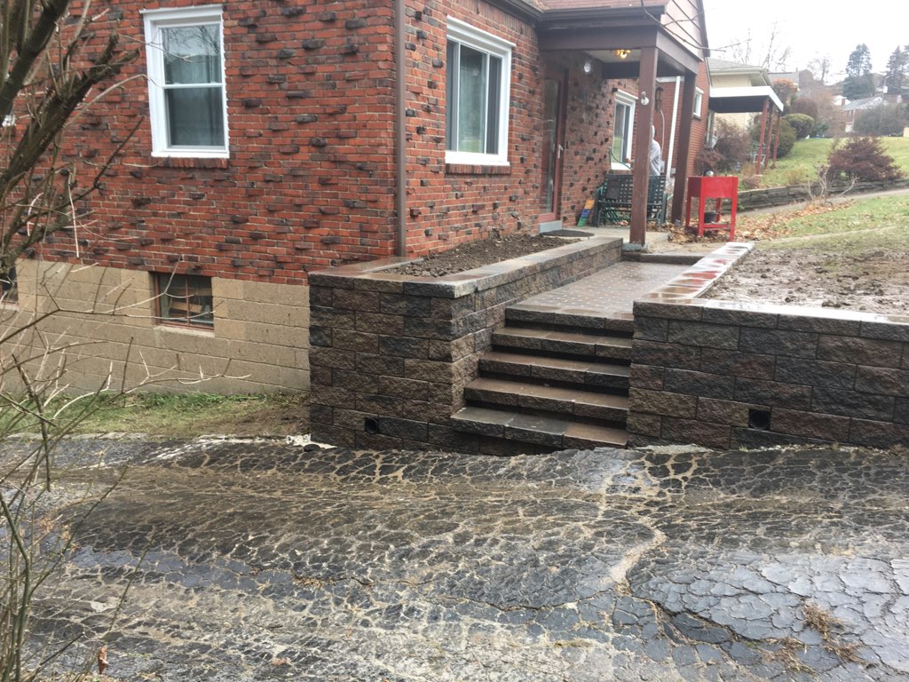 Segmental block retaining wall and matching stone steps leading to a brick home's front porch